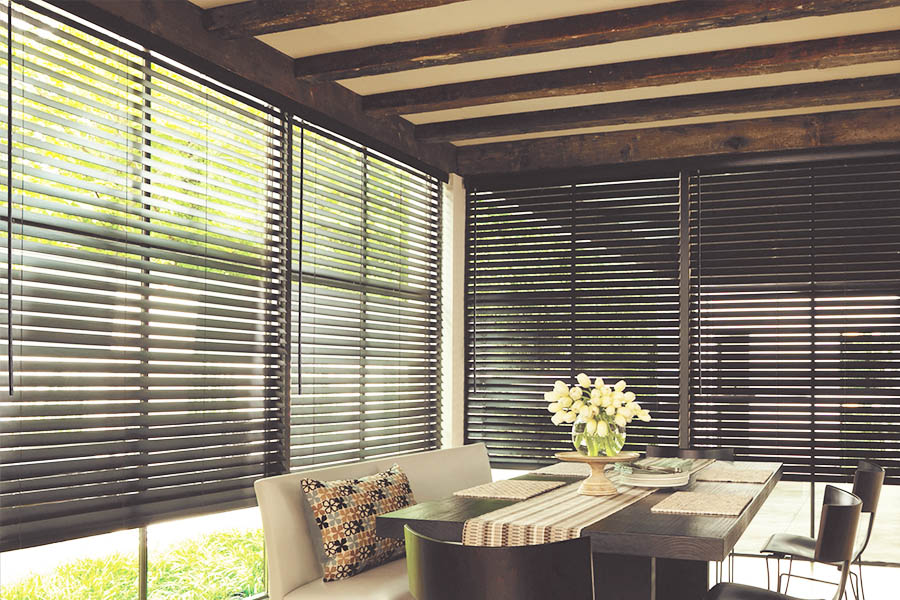 Dark wood window blinds on windows in a sunroom with a dining table